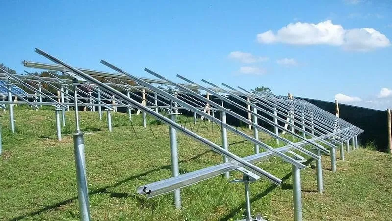 Workers and machinery installing helical screw piles for solar panels at a solar farm construction site.