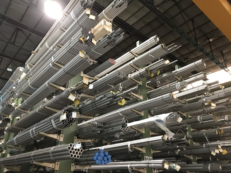 Wide view of metal pipes stacked in an industrial warehouse, emphasizing storage and organization.
