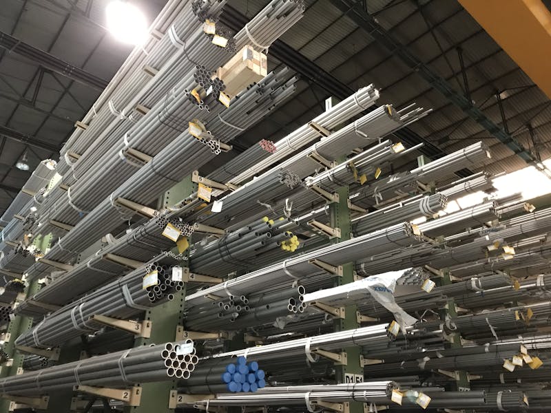 Wide view of metal pipes stacked in an industrial warehouse, emphasizing storage and organization.