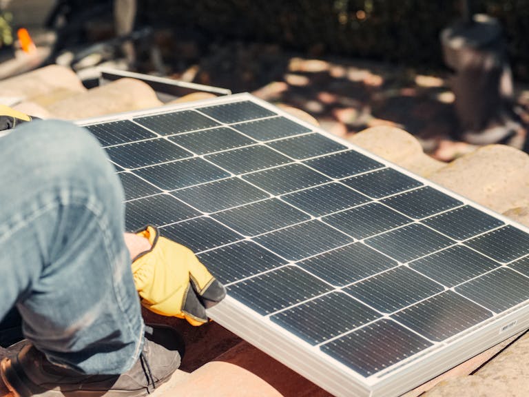 A worker installs a solar panel on a sunlit rooftop, exemplifying renewable energy